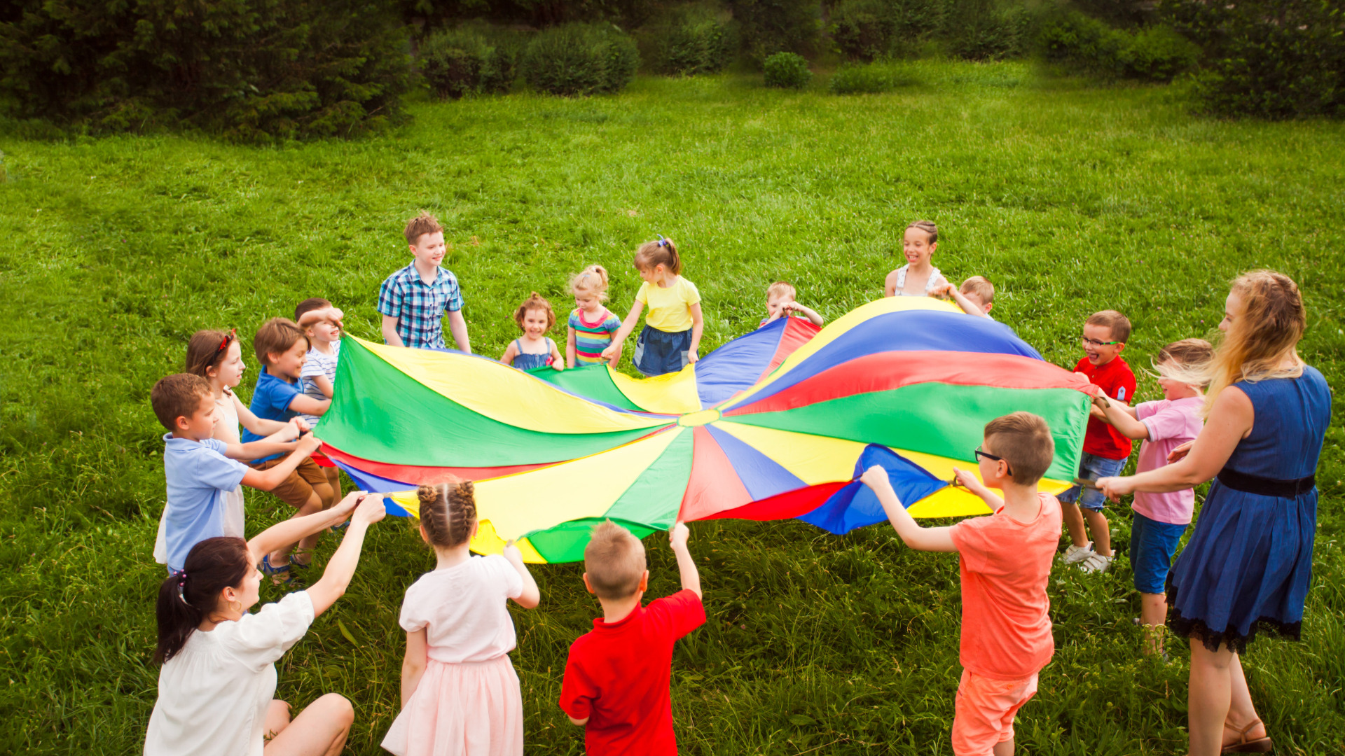 Grupo de niños y niñas con la monitora jugando con un paracaídas