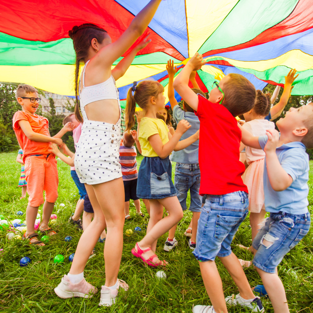 Un grupo de niños y niñas jugando con un paracaídas de colores